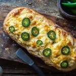 Freshly baked vegan jalapeño cheese artisan bread with golden crust and jalapeño garnish on a wooden board.